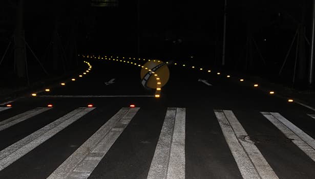 Glowing OEM solar road studs installed on pedestrian crossing at night - High-visibility road safety solution for urban traffic infrastructure projects