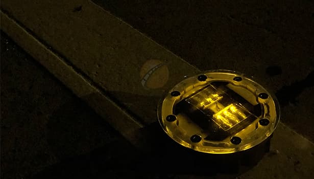 Closeup of round solar cat eye road stud with yellow light