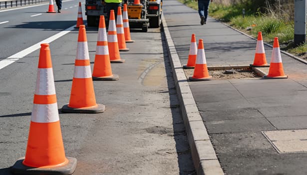 Orange and white traffic cones directing traffic and marking a sidewalk repair area during roadside construction